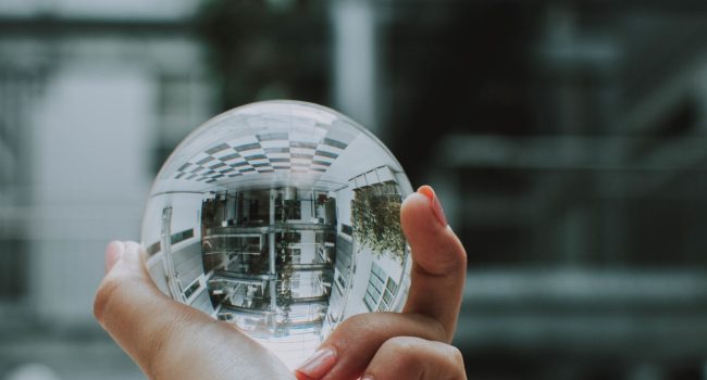 A vertical selective shot of a person holding a clear crystal glass ball with the reflection of a building