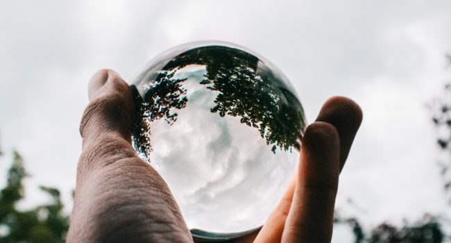 person-holding-glass-ball-with-reflection-beautiful-green-trees-breathtaking-clouds